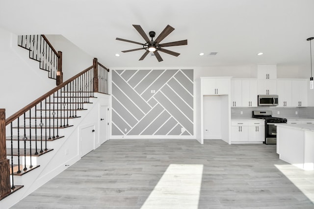 interior space with light hardwood / wood-style flooring, appliances with stainless steel finishes, pendant lighting, ceiling fan, and white cabinets