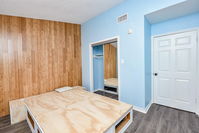 bedroom with dark hardwood / wood-style floors, wooden walls, a closet, and a textured ceiling