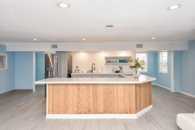 kitchen with a center island, stainless steel fridge with ice dispenser, light hardwood / wood-style flooring, and a textured ceiling