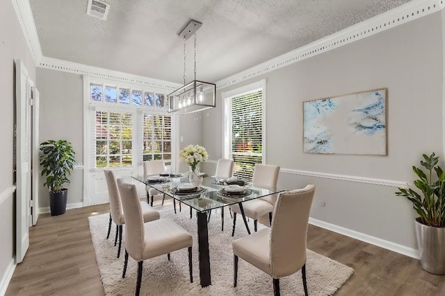 dining space featuring hardwood / wood-style floors, ornamental molding, and a textured ceiling