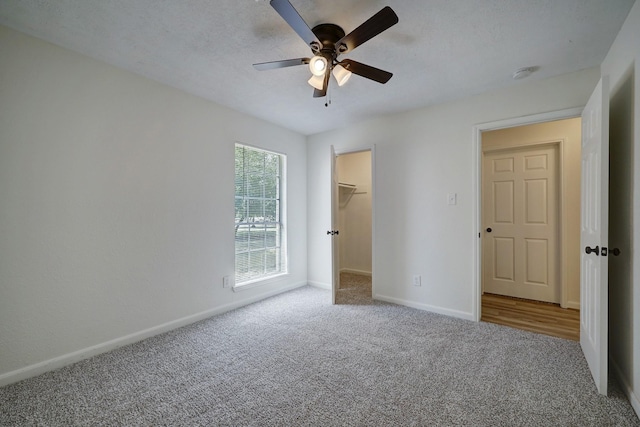 unfurnished bedroom featuring ceiling fan, carpet flooring, a textured ceiling, a spacious closet, and a closet