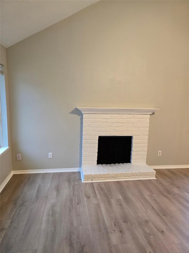 unfurnished living room with vaulted ceiling, a brick fireplace, and light hardwood / wood-style floors