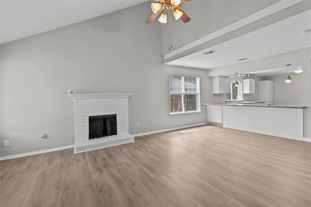 22706 Braken Carter Ln, Katy, TX 77449 - unfurnished living room with a ceiling fan, light wood-style floors, a fireplace, and a towering ceiling