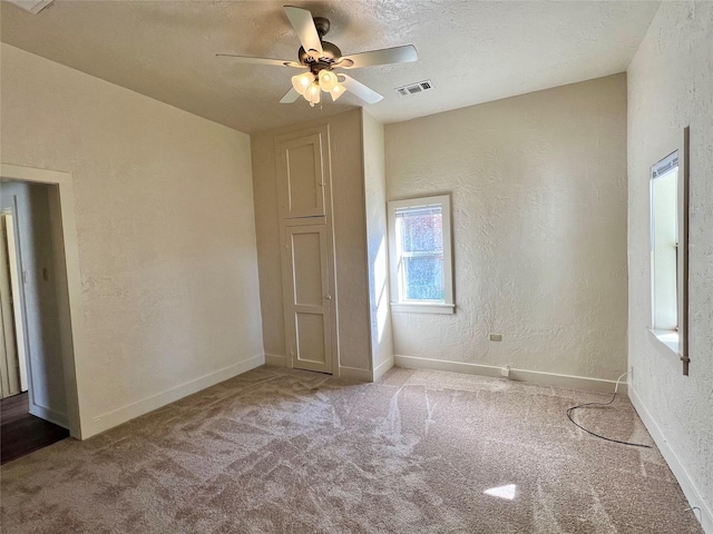 spare room featuring ceiling fan, light colored carpet, and a textured ceiling