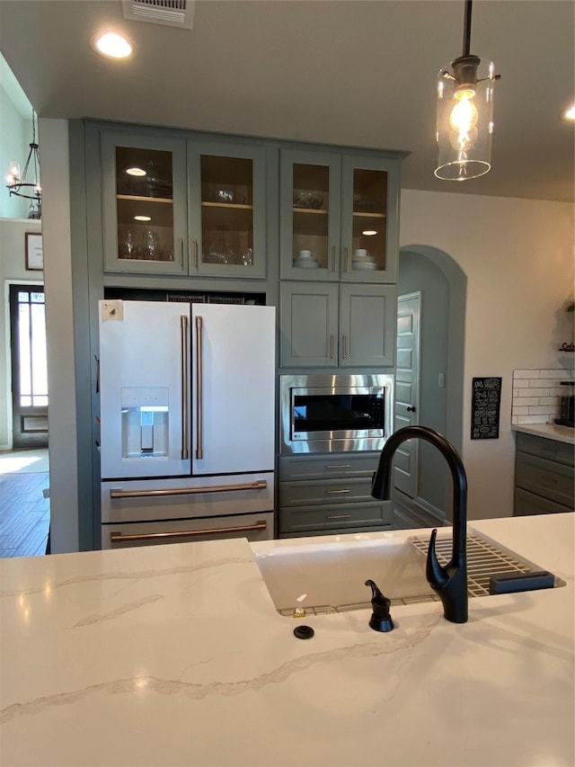 kitchen featuring gray cabinets, hanging light fixtures, stainless steel microwave, high end white refrigerator, and light stone countertops