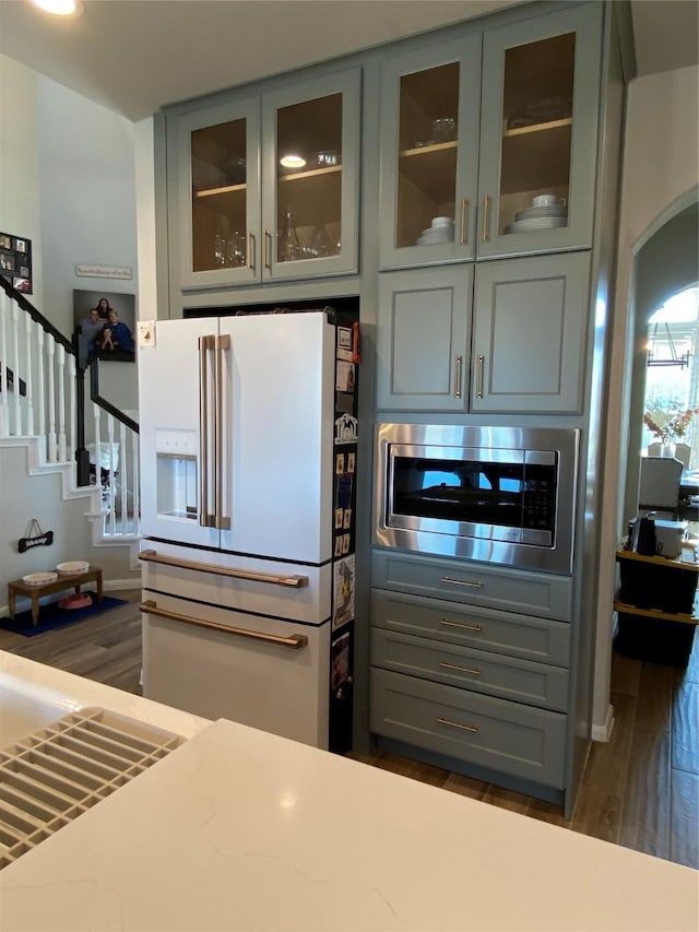 kitchen with gray cabinetry, stainless steel microwave, dark wood-type flooring, and white fridge with ice dispenser