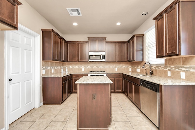 kitchen featuring sink, light tile patterned floors, appliances with stainless steel finishes, a kitchen island, and light stone countertops