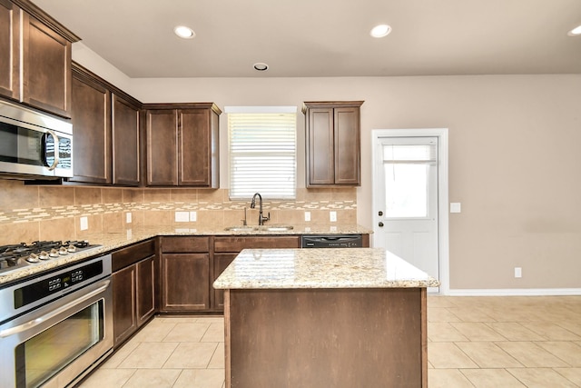 kitchen featuring light tile patterned flooring, sink, light stone counters, a center island, and appliances with stainless steel finishes