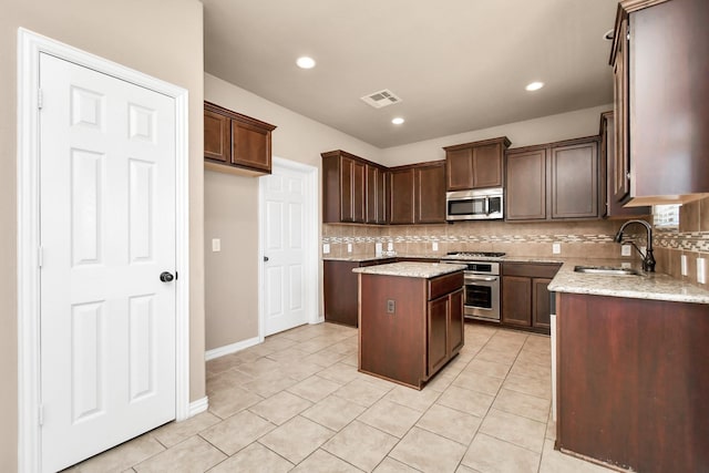 kitchen featuring sink, light tile patterned floors, appliances with stainless steel finishes, a kitchen island, and light stone countertops