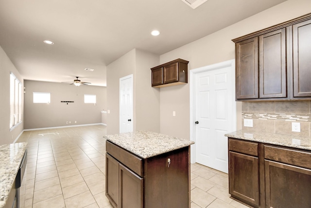 kitchen with light tile patterned flooring, tasteful backsplash, ceiling fan, light stone counters, and dark brown cabinets