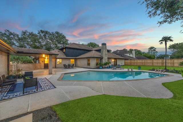 pool at dusk with a patio and a lawn