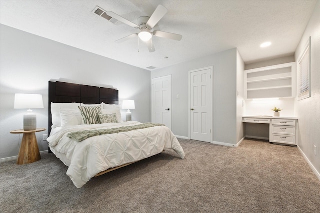 carpeted bedroom with a textured ceiling, built in desk, and ceiling fan