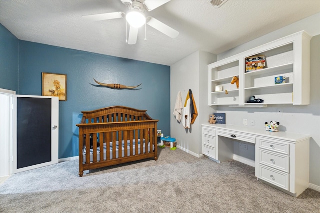 bedroom featuring built in desk, light colored carpet, ceiling fan, a crib, and a textured ceiling