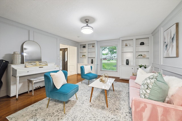 living area with built in shelves, ornamental molding, a textured ceiling, and hardwood / wood-style flooring