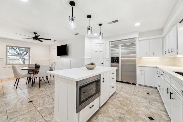 kitchen with pendant lighting, white cabinetry, backsplash, a center island, and built in appliances