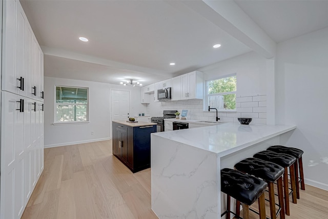 kitchen with a kitchen bar, white cabinetry, light hardwood / wood-style flooring, kitchen peninsula, and black appliances