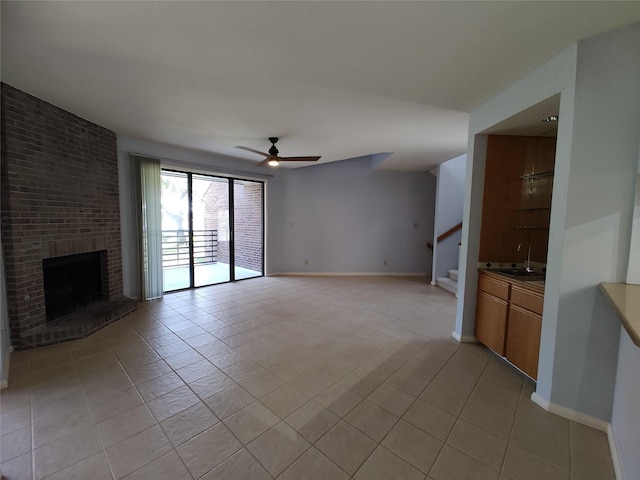 unfurnished living room featuring sink, a fireplace, ceiling fan, and light tile patterned flooring