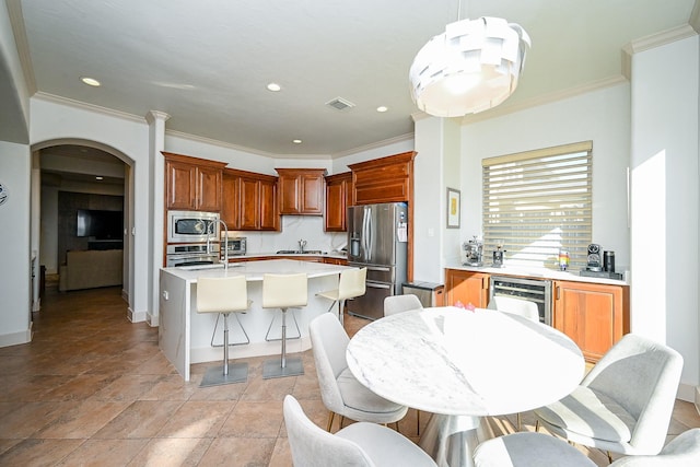 kitchen featuring appliances with stainless steel finishes, pendant lighting, an island with sink, beverage cooler, and decorative backsplash