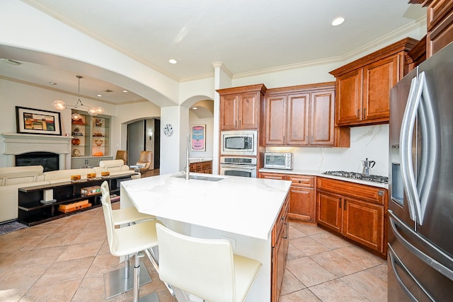 kitchen with sink, a kitchen island with sink, stainless steel appliances, a kitchen bar, and decorative light fixtures