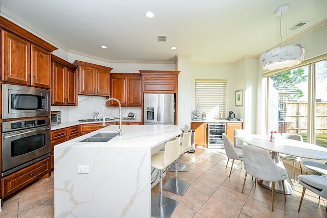 kitchen with beverage cooler, hanging light fixtures, ornamental molding, stainless steel appliances, and a center island with sink