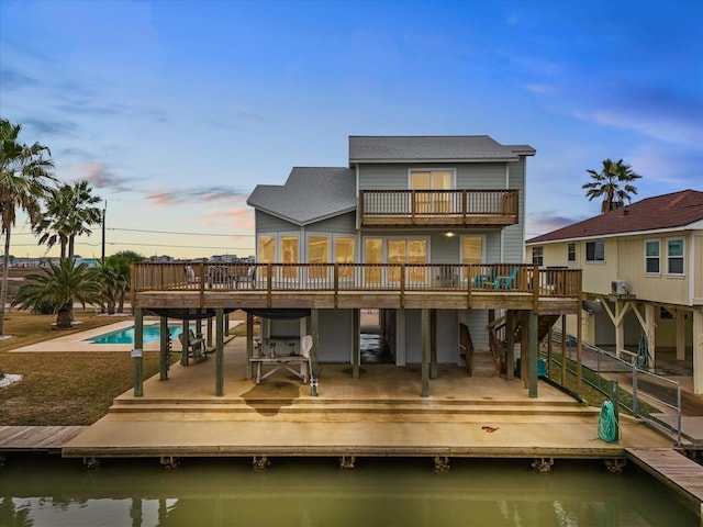 back house at dusk featuring a swimming pool side deck with water view, a balcony, and a patio