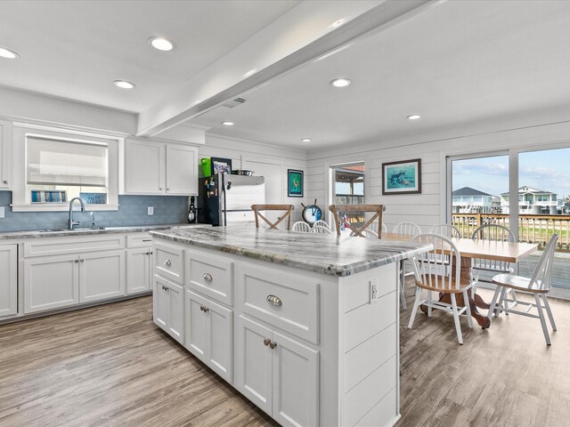 kitchen with sink, stainless steel refrigerator, white cabinetry, a center island, and light stone counters