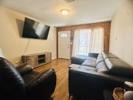 living room with light hardwood / wood-style flooring, a textured ceiling, and brick wall