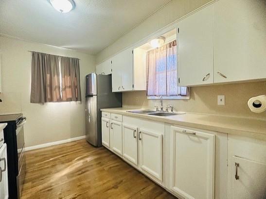 kitchen with white cabinetry, wood-type flooring, sink, and stainless steel fridge