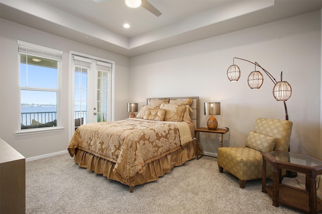 carpeted bedroom with a raised ceiling, a water view, access to outside, and ceiling fan