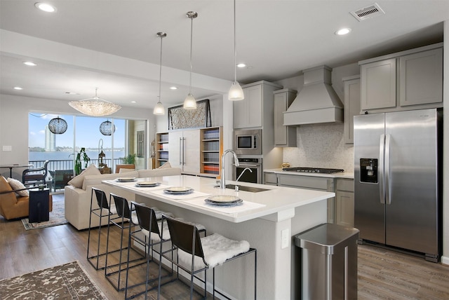 kitchen featuring pendant lighting, premium range hood, gray cabinetry, built in appliances, and a center island with sink