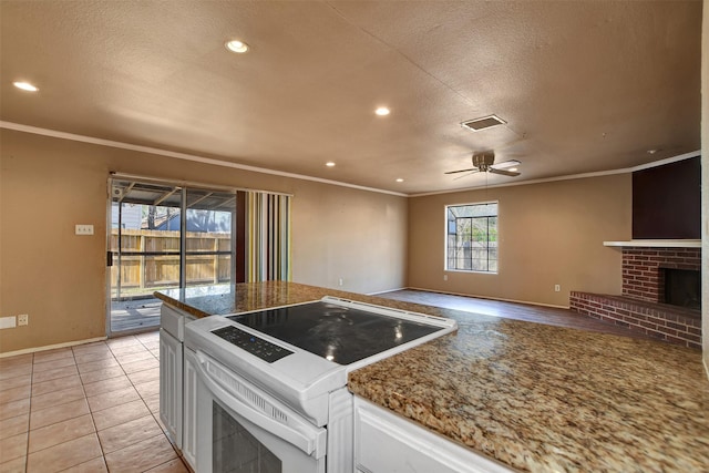 kitchen featuring white electric range, white cabinetry, a textured ceiling, light tile patterned floors, and a fireplace