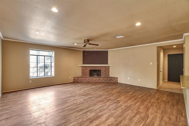 unfurnished living room with ceiling fan, a fireplace, ornamental molding, a textured ceiling, and light wood-type flooring