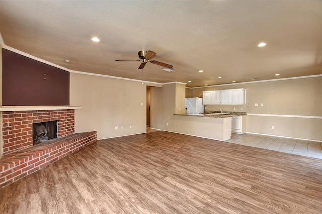 unfurnished living room with ceiling fan, ornamental molding, light hardwood / wood-style floors, and a brick fireplace