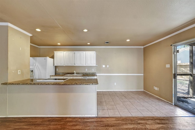 kitchen featuring sink, light tile patterned floors, kitchen peninsula, white fridge with ice dispenser, and white cabinets