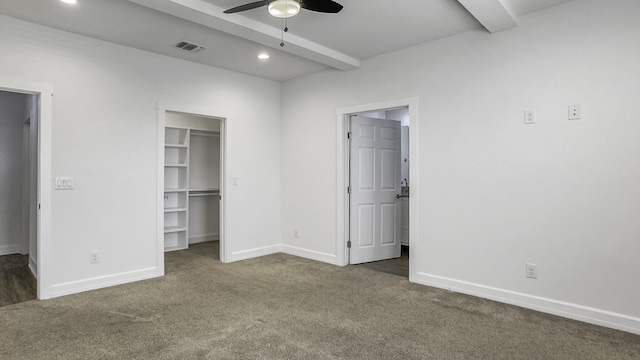 unfurnished bedroom with beamed ceiling, ceiling fan, a spacious closet, and dark carpet