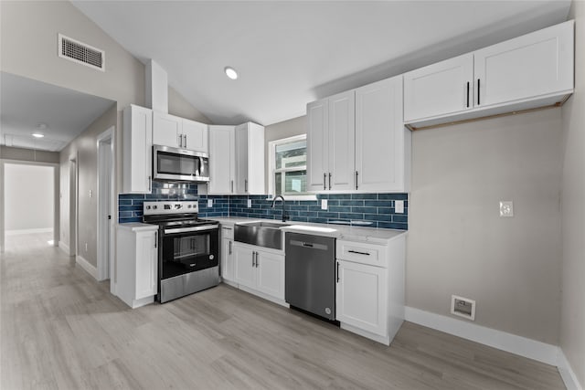 kitchen with vaulted ceiling, tasteful backsplash, white cabinetry, sink, and stainless steel appliances