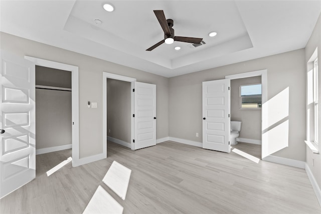 unfurnished bedroom with light hardwood / wood-style flooring, ceiling fan, ensuite bathroom, a raised ceiling, and a closet