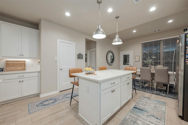 kitchen featuring pendant lighting, white cabinetry, backsplash, a center island, and a kitchen bar