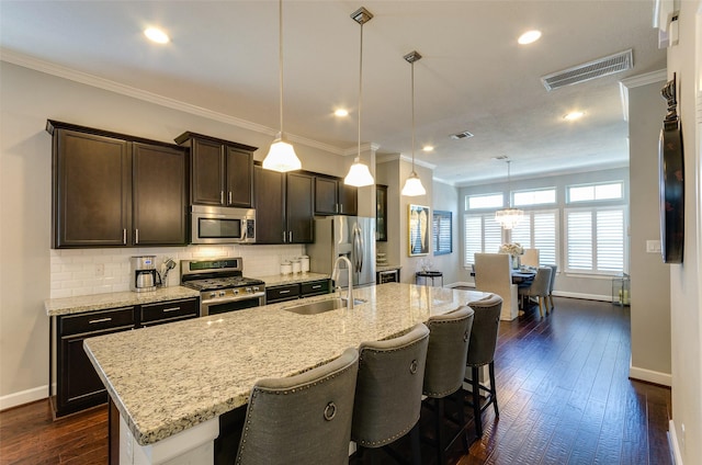 kitchen with an island with sink, appliances with stainless steel finishes, decorative light fixtures, and sink