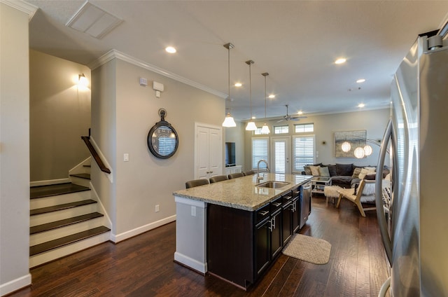 kitchen with sink, hanging light fixtures, light stone counters, stainless steel appliances, and a center island with sink