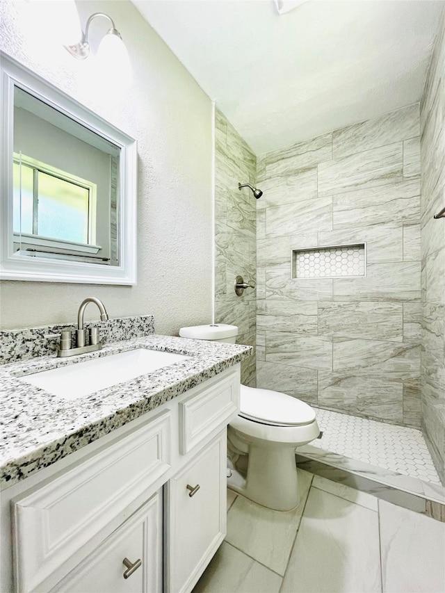 bathroom with a tile shower, vanity, and toilet