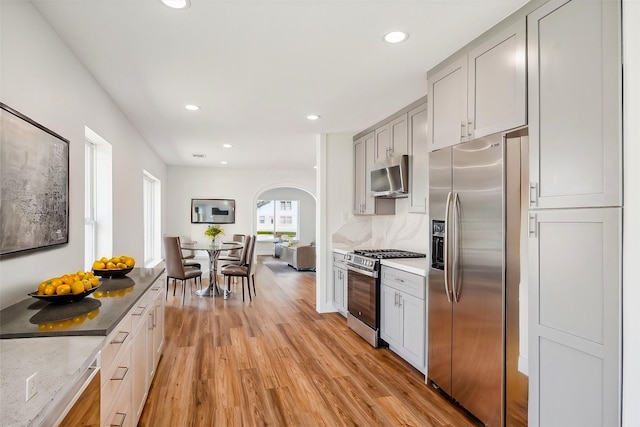 kitchen with gray cabinetry, stainless steel appliances, light stone countertops, light hardwood / wood-style floors, and decorative backsplash