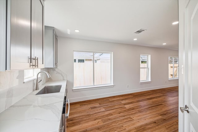 kitchen with light stone counters, sink, decorative backsplash, and hardwood / wood-style floors