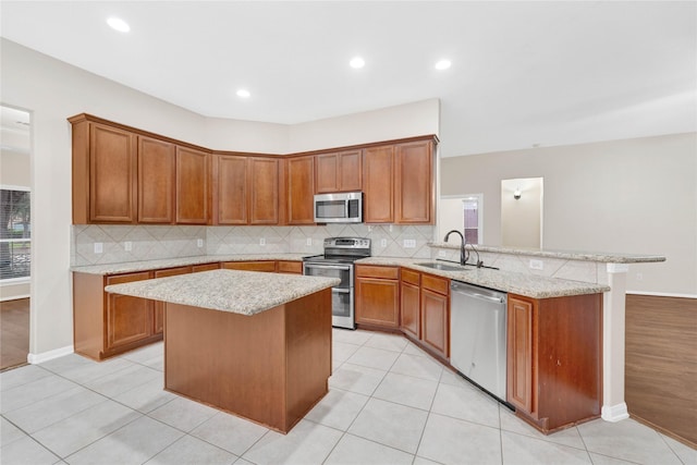 kitchen with appliances with stainless steel finishes, sink, light stone counters, and kitchen peninsula