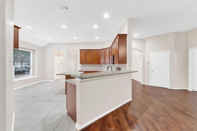 kitchen with sink, backsplash, light stone counters, kitchen peninsula, and light wood-type flooring