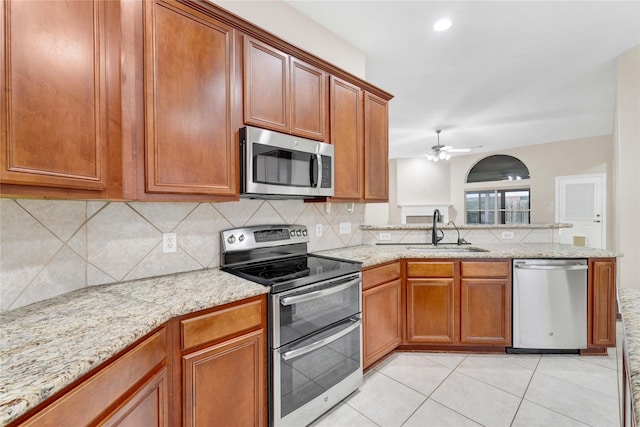 kitchen with sink, light tile patterned floors, appliances with stainless steel finishes, ceiling fan, and light stone countertops