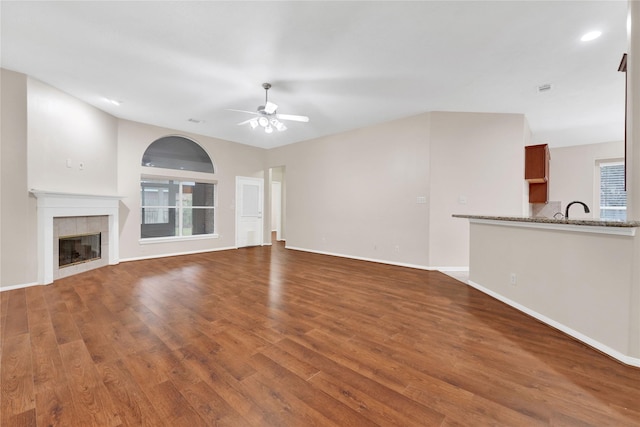 unfurnished living room featuring sink, hardwood / wood-style flooring, a tile fireplace, and ceiling fan