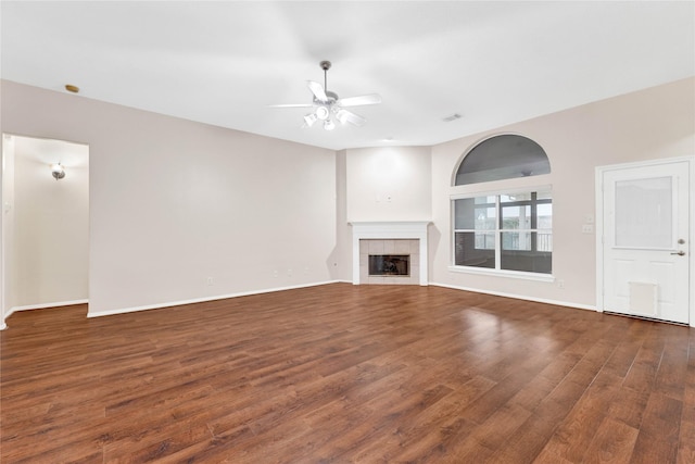 unfurnished living room featuring a tiled fireplace, dark wood-type flooring, and ceiling fan