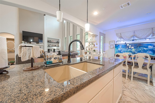 kitchen featuring sink, pendant lighting, white cabinets, and dark stone counters