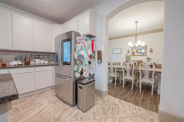 kitchen with hanging light fixtures, stainless steel fridge, white cabinets, and backsplash